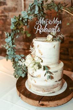 a wedding cake sitting on top of a wooden table next to a greenery wreath