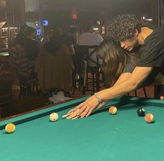 a man and woman leaning over a pool table with balls in front of them,