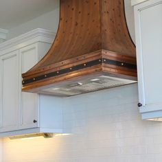 a kitchen with white cabinets and a wooden stove hood over the range in the center