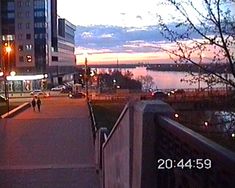 people walking down a sidewalk next to a body of water at night with the sun setting