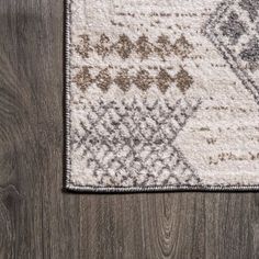 a white rug with brown and beige designs on top of wooden flooring next to a gray wall