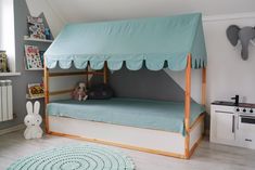 a child's bed with a blue canopy over it and a stuffed animal on the floor