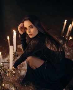 a woman sitting in front of candles with one hand on her head and looking at the camera