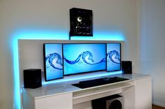 two computer monitors sitting on top of a white desk in front of a blue light