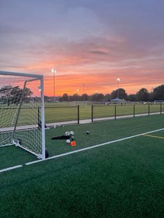 a soccer goal with the sun setting in the background and some balls on the ground