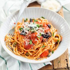 a white bowl filled with pasta and sauce on top of a wooden cutting board next to a fork