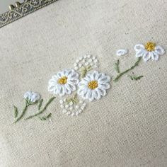 some white daisies are on a beige cloth with green stems and yellow centers in the middle