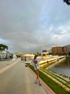 a woman is standing on the side walk with a rainbow in the sky above her