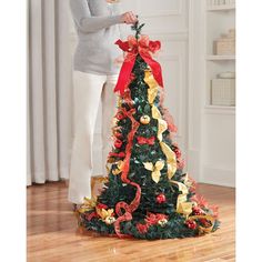 a woman decorating a christmas tree with red and gold ribbons on it's top