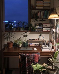 a desk with books and plants on it next to a window in a room that has a view of the city outside