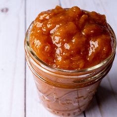 a glass jar filled with food sitting on top of a white wooden table next to a spoon