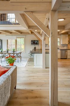 an open living room and dining area with wood flooring, exposed beams, and white walls