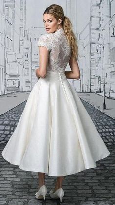 a woman standing in front of a wall wearing a white dress with lace on it