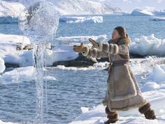 a woman standing in the snow next to an icy lake and holding out her hand