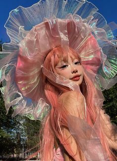 a woman with long pink hair wearing a large plastic hat and holding her hands behind her back