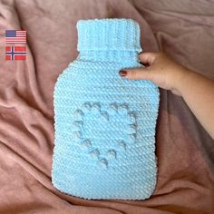 a crocheted blue bottle with the word love written on it and a person's hand holding one