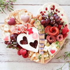 a heart shaped platter filled with different types of cheeses and crackers next to grapes