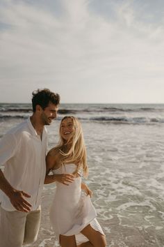 a man and woman are standing on the beach smiling at each other as they walk towards the water