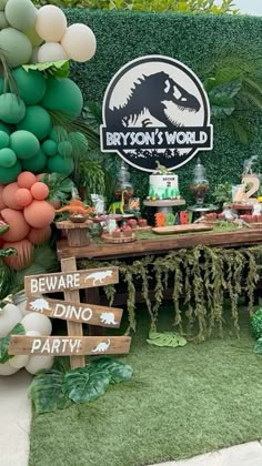 an outdoor party with balloons and decorations on the grass, including a sign that says beware dinos world