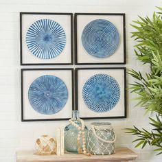 four blue and white circular artwork hanging on a wall above a table with vases