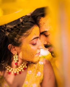 a man and woman dressed in yellow are kissing under an orange canopy with their eyes closed