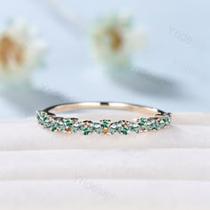 a wedding band with green and white stones in the center on top of a cloth