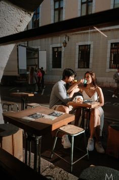 two people sitting at a table eating food in an open air area with tables and chairs