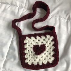 a crocheted bag sitting on top of a white bed covered in blankets and pillows