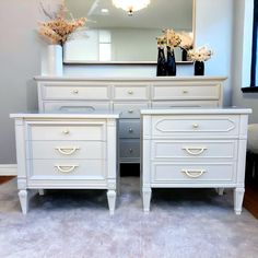 two white dressers and a mirror in a room with carpeting on the floor