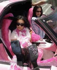 two women sitting in a pink car with their feet up on the seat and one is wearing sunglasses