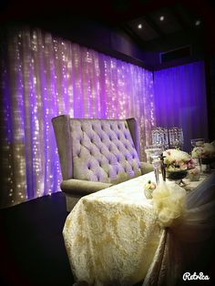 a chair and table in front of a purple curtain with lights on the wall behind it