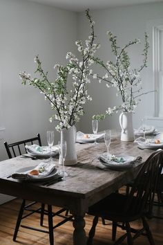 a dining room table with flowers in vases and plates on the wooden table top