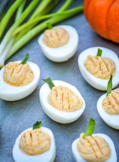 several deviled eggs are arranged on a table with green onions and pumpkins in the background