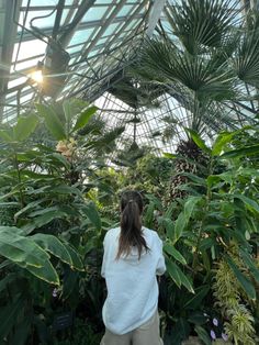 a woman in white shirt and khaki pants looking at plants inside a greenhouse