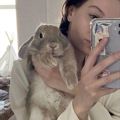 a woman taking a selfie with her phone and holding a rabbit in front of her face