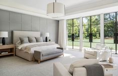 a large bedroom with two chairs and a bed in it's center area, along with windows that look out onto a grassy field