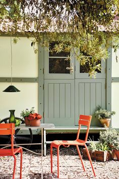 an outdoor table and chairs in front of a house with potted plants on the side