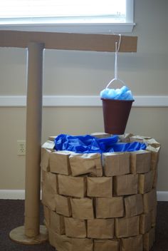 a cardboard basket that is sitting on the ground next to a pole with a bucket in it