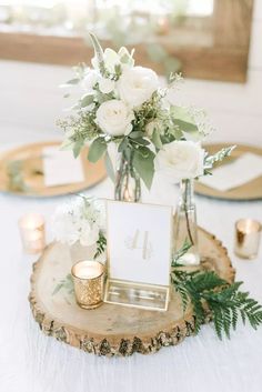 a centerpiece with white flowers and greenery sits on a wood slice at the head table