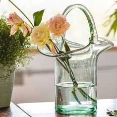 some flowers are in a glass pitcher on a table next to a potted plant