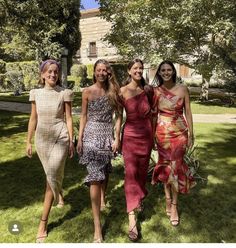 four women in dresses are walking on the grass