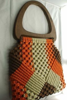 a crocheted purse hanging on a white wall in front of a window with a wooden handle