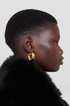 a woman with short hair wearing gold earrings and black fur collar, looking off to the side