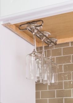 three wine glasses are hanging from the ceiling in front of a brick wall and wooden shelf