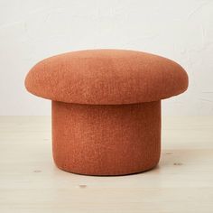 an orange round ottoman sitting on top of a wooden table next to a white wall