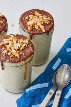 three jars filled with chocolate and nuts on top of a blue towel next to two spoons