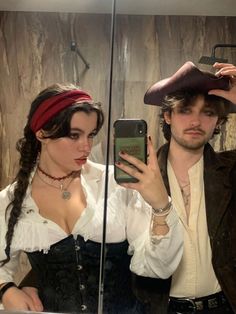 a man and woman dressed up in pirate costumes looking at their cell phones while standing next to each other