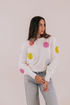 a woman wearing a white sweater with colorful flowers on it