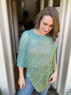 a woman standing in front of a door wearing a green crocheted ponchy