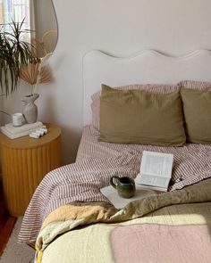 a bed with a book and cup on top of it next to a plant in a vase